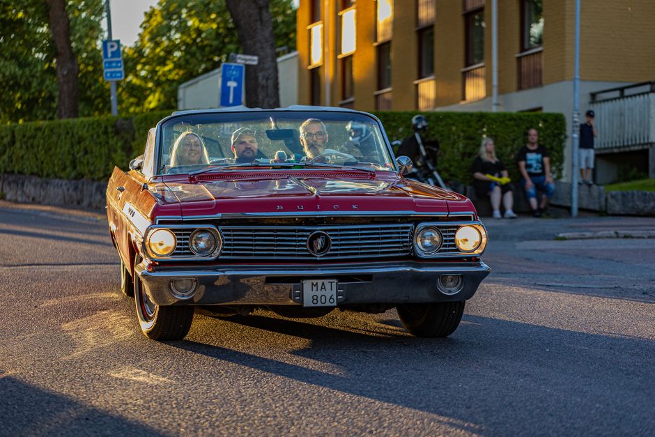 A classic red Buick LeSabre drives through city streets at sunset, capturing the retro charm of vintage cars.